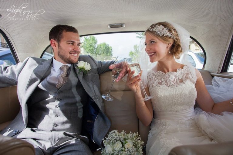 beautiful wedding couple inside wedding car with champagne glasses